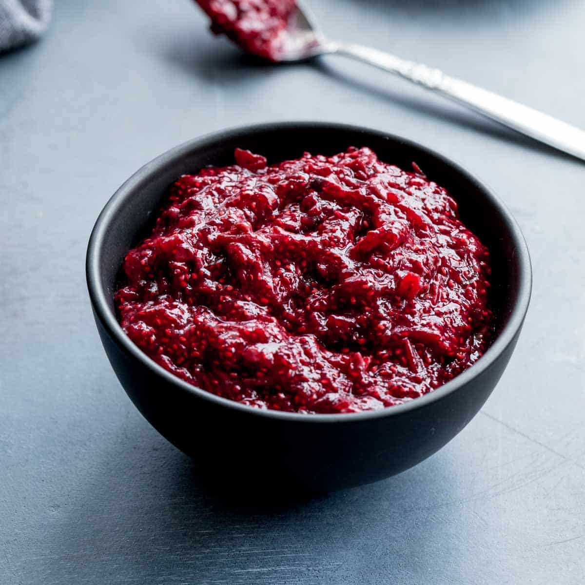 Angled view of healthy cranberry sauce in a small black bowl with a spoon in the background.