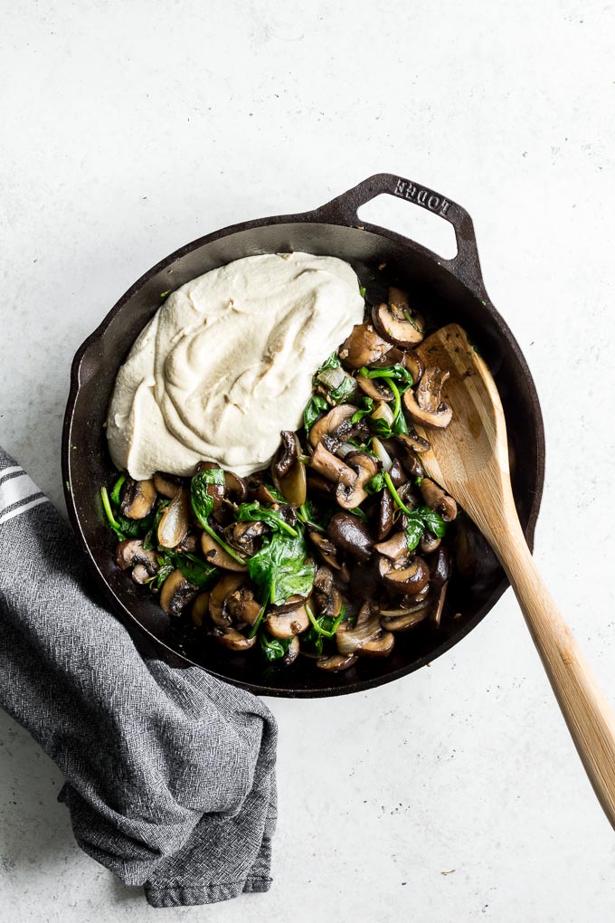 Overhead view of mushroom spinach filling and cashew cream in a cast iron skillet.