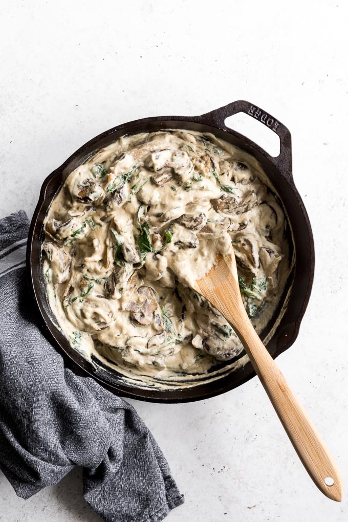 Overhead view of mushroom spinach dip in a cast iron skillet with a wooden spoon inserted into it.