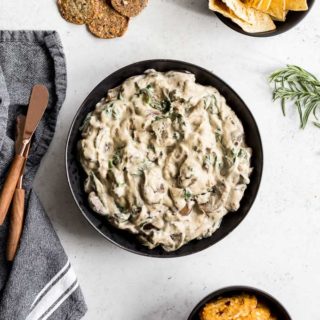 Overhead view of Mushroom Spinach Dip in a black bowl with chips, pretzels and crackers off to the side.