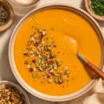 A bowl of roasted red pepper and butternut squash soup with toppings on the side.