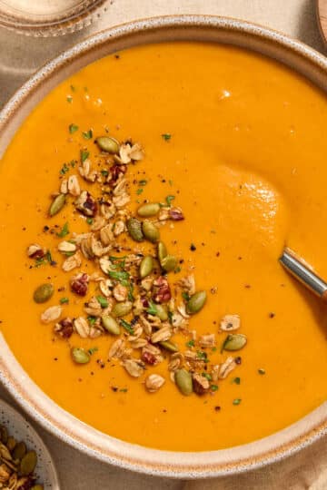 A bowl of roasted red pepper and butternut squash soup with toppings on the side.