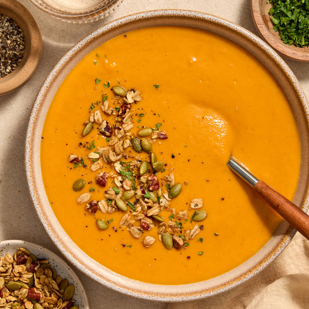 A bowl of roasted red pepper and butternut squash soup with toppings on the side.