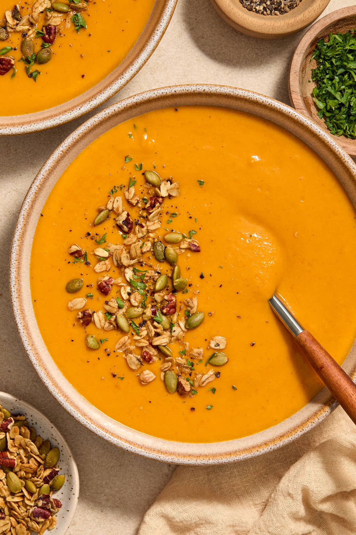 Close up of a bowl of soup with a spoon inserted into it and toppings on the side.