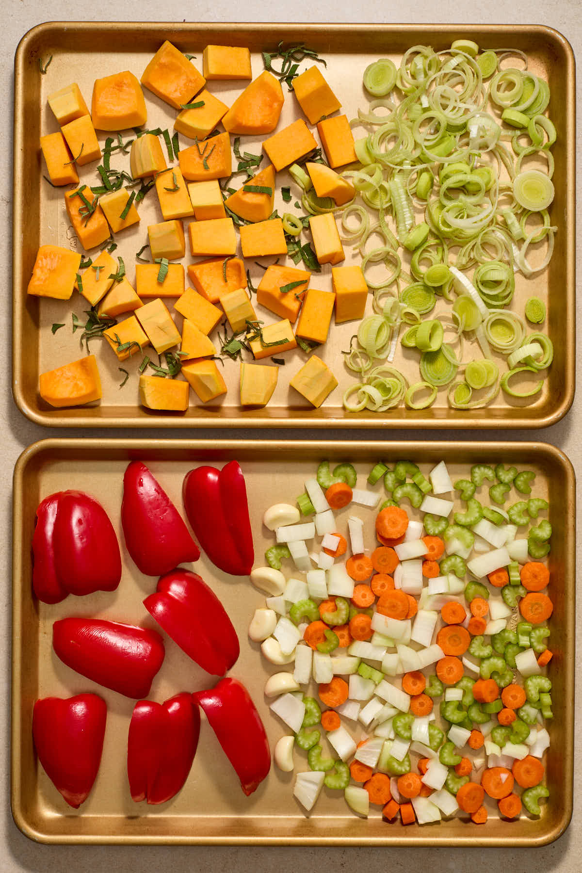 Chopped squash and vegetables arranged on two sheet pans.