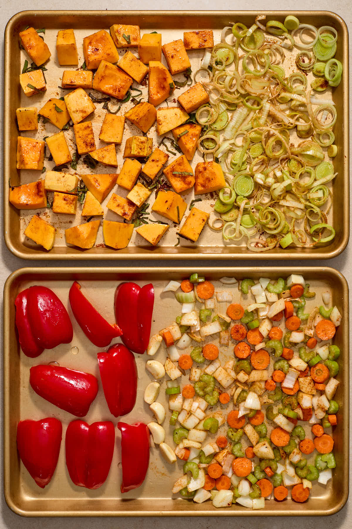 Squash and vegetables tossed with oil and seasonings on the sheet pans.