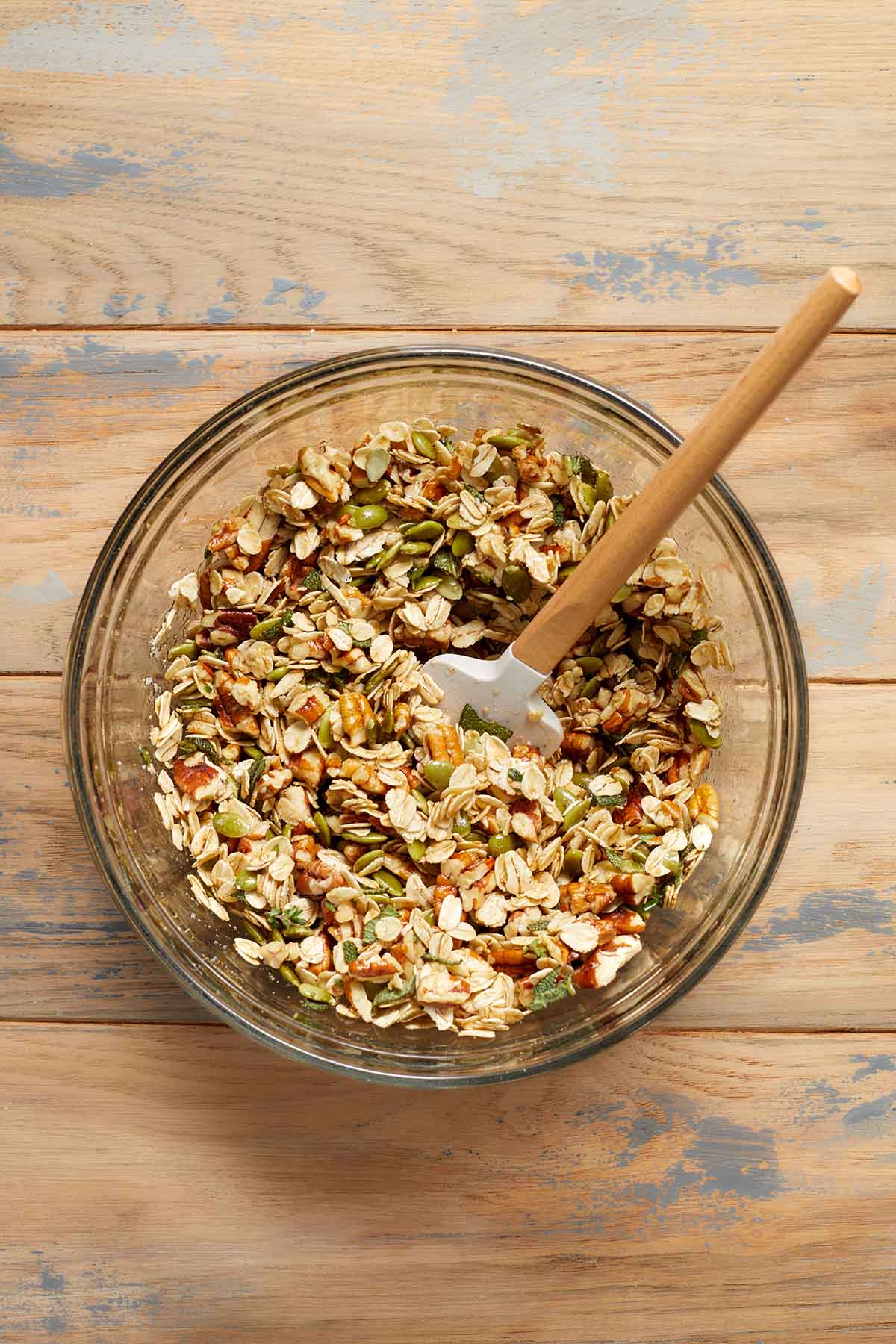 Granola ingredients mixed together in a glass bowl with a spatula.