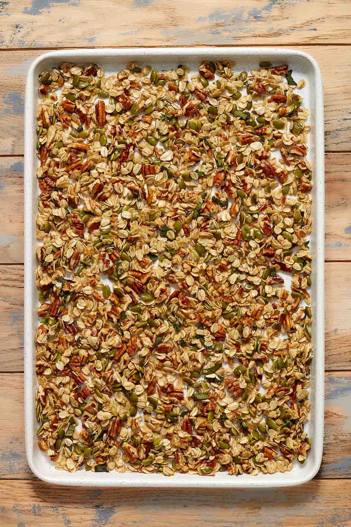 Granola mixture spread out on a large baking sheet.