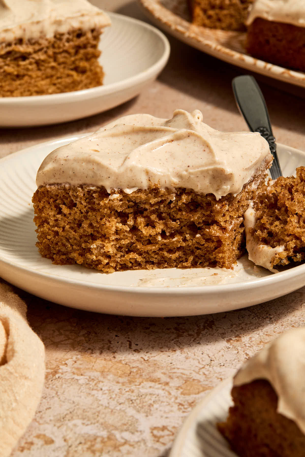 A piece of chai cake on a plate with a forkful removed and other pieces on plates in the background.