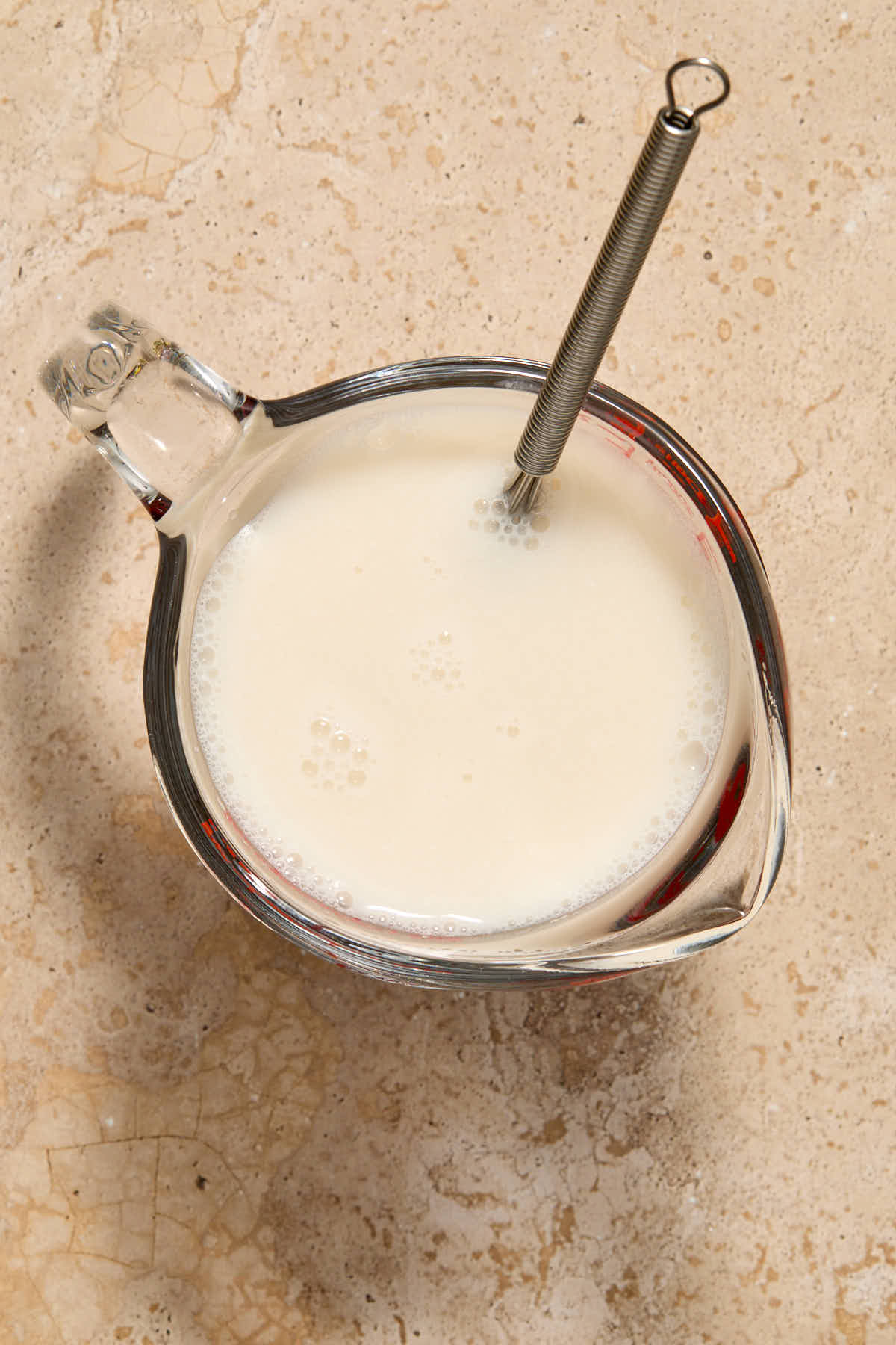 Almond milk and vinegar mixed together with a whisk in a glass measuring cup.
