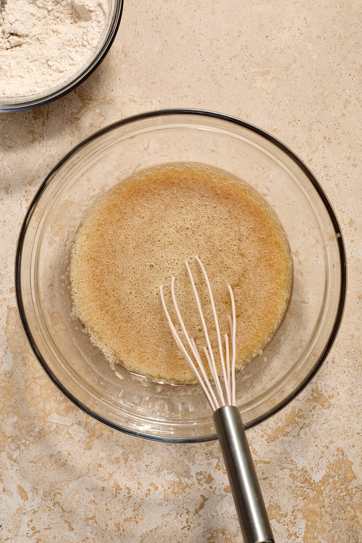 Wet ingredients whisked together in a glass bowl with dry ingredients off to the side.