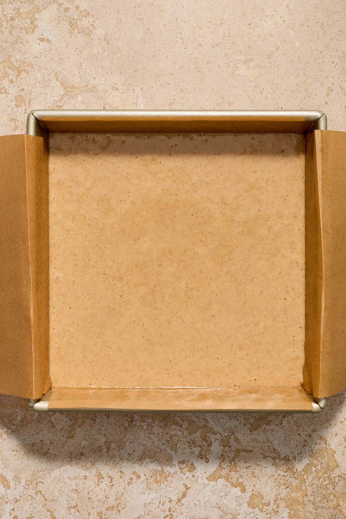 Batter spread out in the prepared square cake pan.
