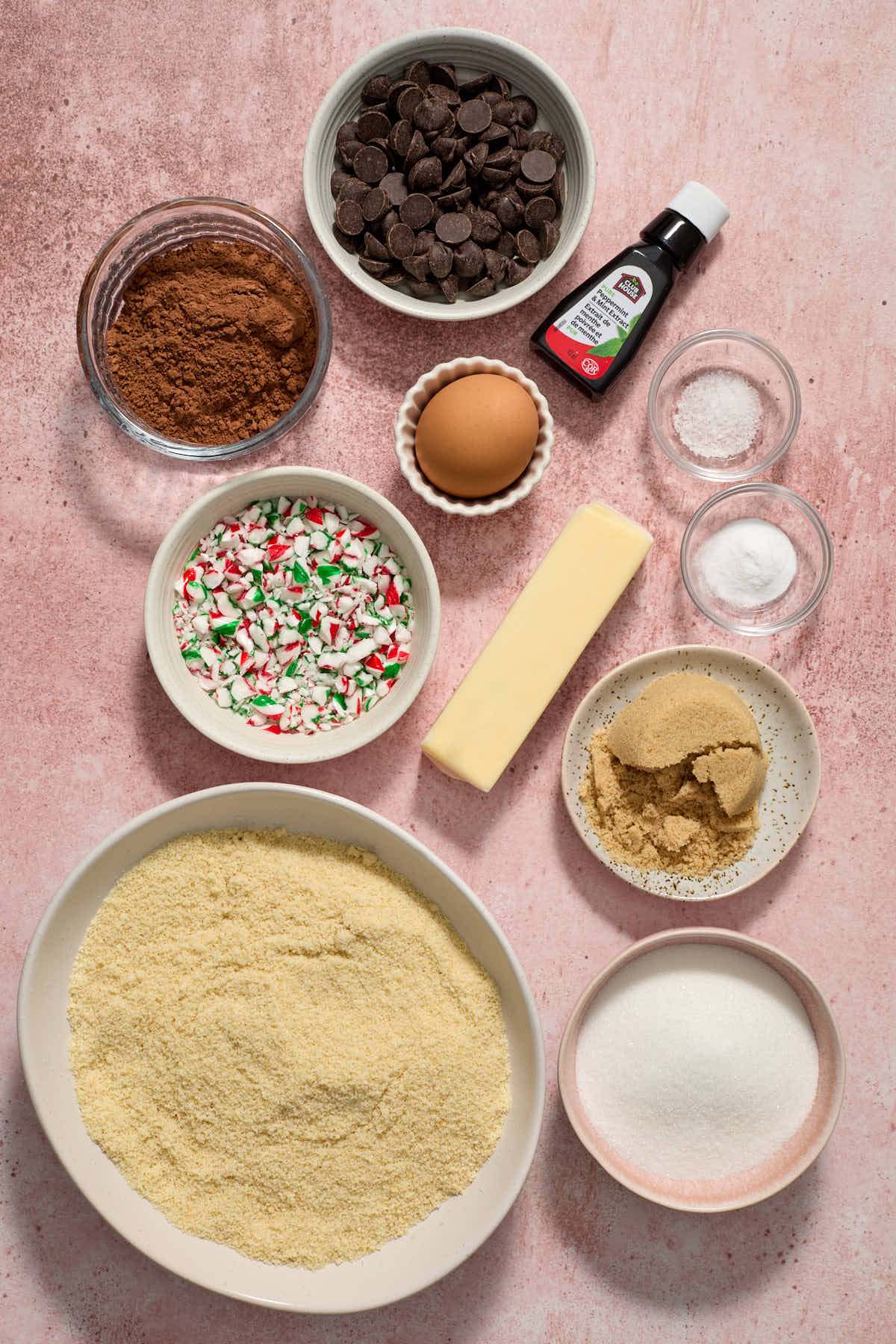 Ingredients to make double chocolate peppermint cookies arranged on a pink surface.