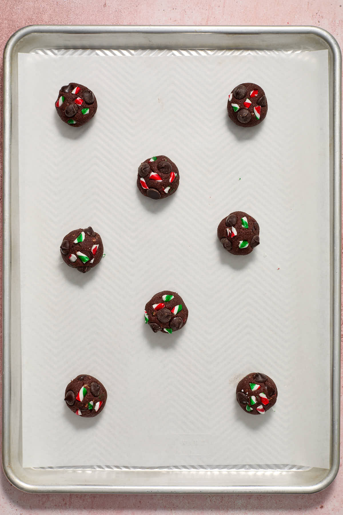 Eight cookie dough balls arranged on a parchment lined baking sheet.