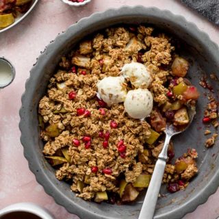 Apple cranberry crisp in a grey pie plate with scoops of crisp taken out and a cup of coffee off to the side.