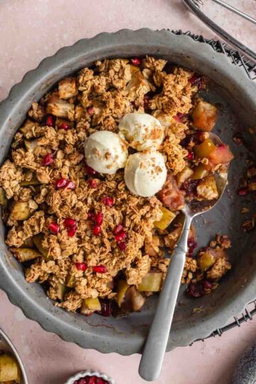 Overhead of cranberry apple crisp in a pie dish with some removed and ice cream on top.