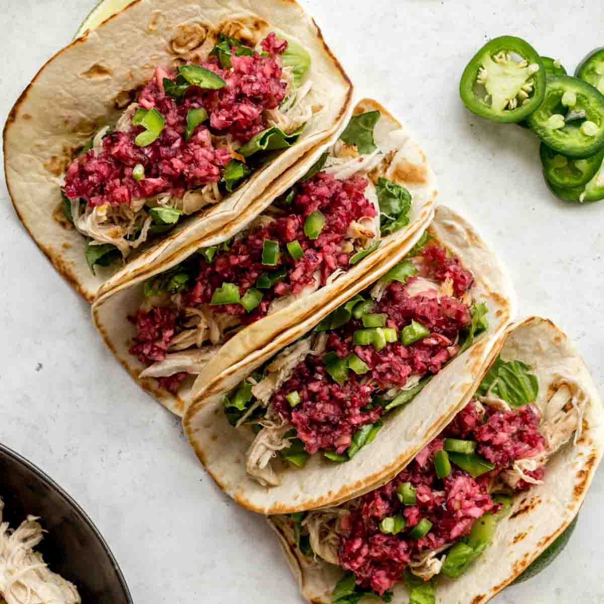 Overhead of 4 apple cranberry chicken tacos topped with cranberry salsa.