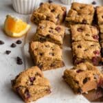 Angled view of cranberry chocolate chip cookie bars arranged on white parchment paper.