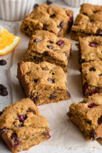 Angled view of cranberry chocolate chip cookie bars arranged on white parchment paper.