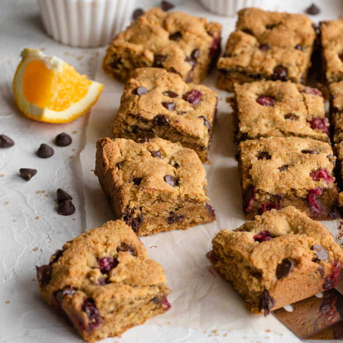 Angled view of cranberry chocolate chip cookie bars arranged on white parchment paper.