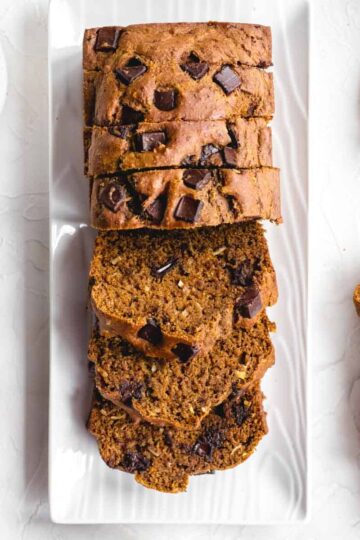 Overhead of whole wheat pumpkin bread sliced on a white platter.
