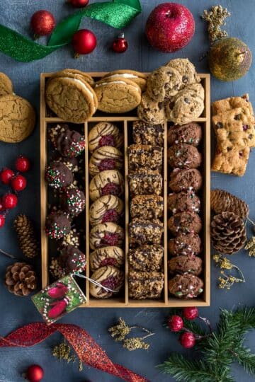 Overhead view of Christmas cookies arranged in a box on a dark surface.