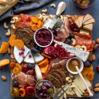 Overhead view of fully assembled cheese board on a dark surface with bread and wine off to the sides.