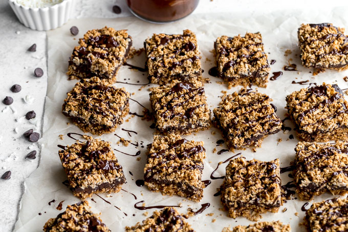 Chocolate oat squares drizzled with chocolate and arranged on a sheet of parchment paper.