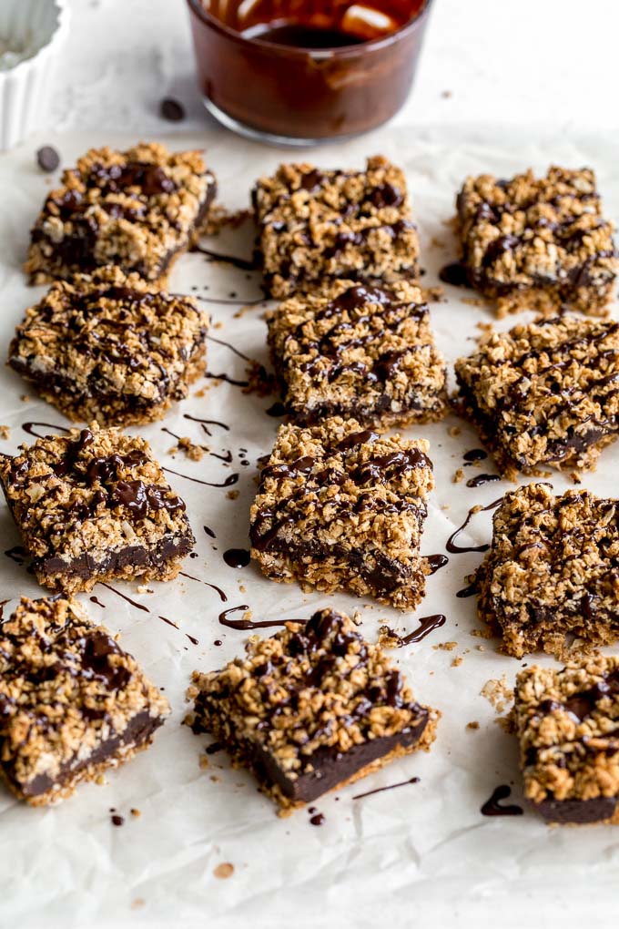 Chocolate crumble bars resting on parchment paper with a bowl of chocolate in the background.