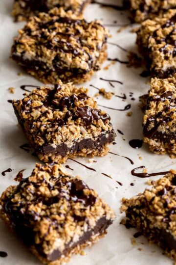 Angled view of chocolate oat bars on parchment paper with melted chocolate drizzled over top.