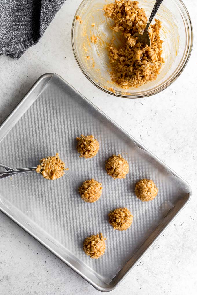 Peanut butter balls being scooped onto a baking sheet.