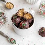 Overhead of peanut butter balls topped with Christmas sprinkles and piled into a white mug.