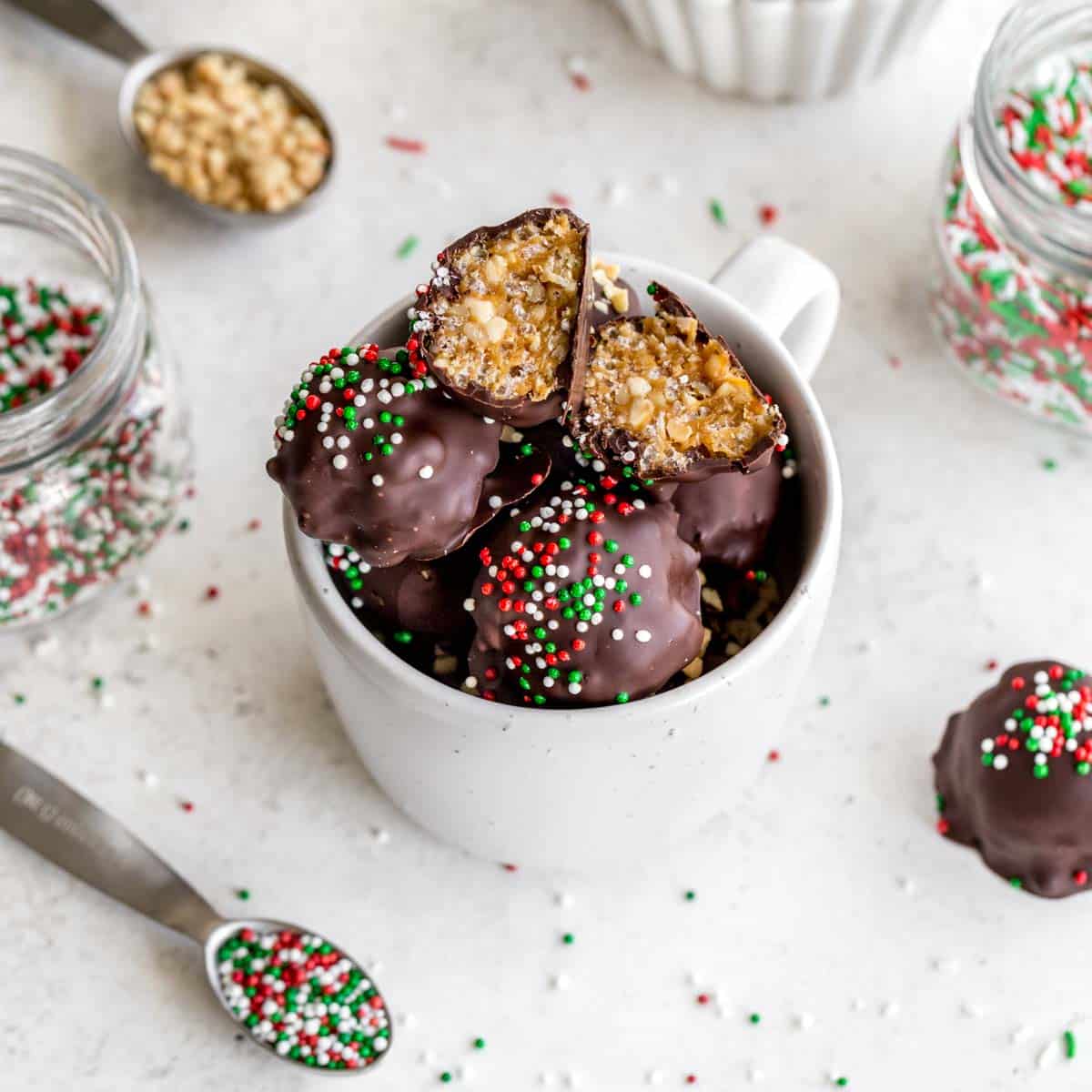 Overhead of peanut butter balls topped with Christmas sprinkles and piled into a white mug.