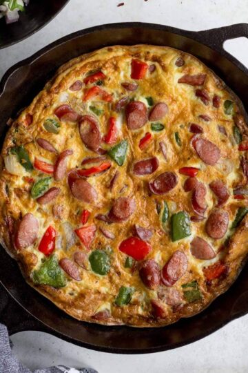 Sausage frittata with peppers and onions in a black cast iron skillet.