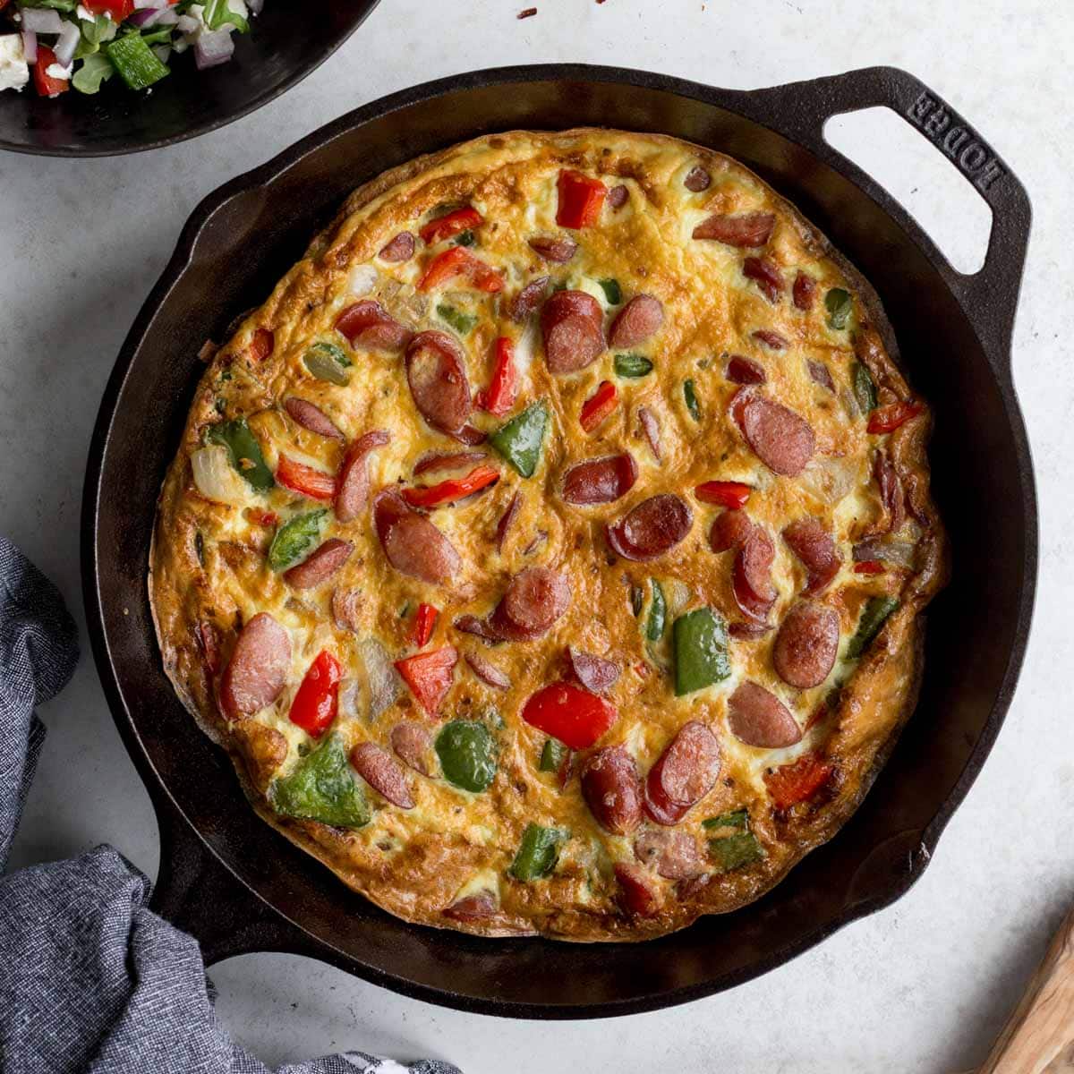 Sausage frittata with peppers and onions in a black cast iron skillet.