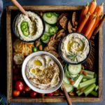 White bean dips arranged in a wooden tray with crackers and veggies for dipping.