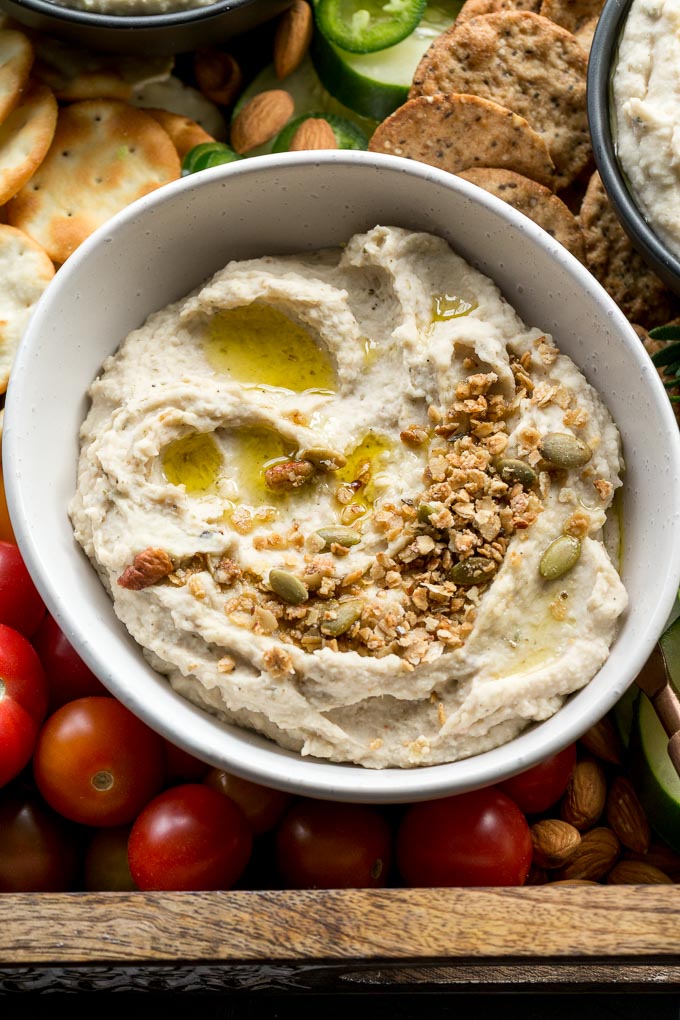 Up-close view of garlic herb white bean dip in a white bowl and topped with oil and granola.