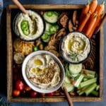 Overhead of 3 variations of white bean dip served with crackers and veggies.