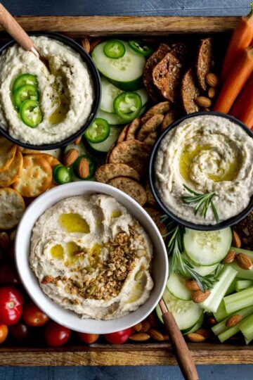Overhead of 3 variations of white bean dip served with crackers and veggies.