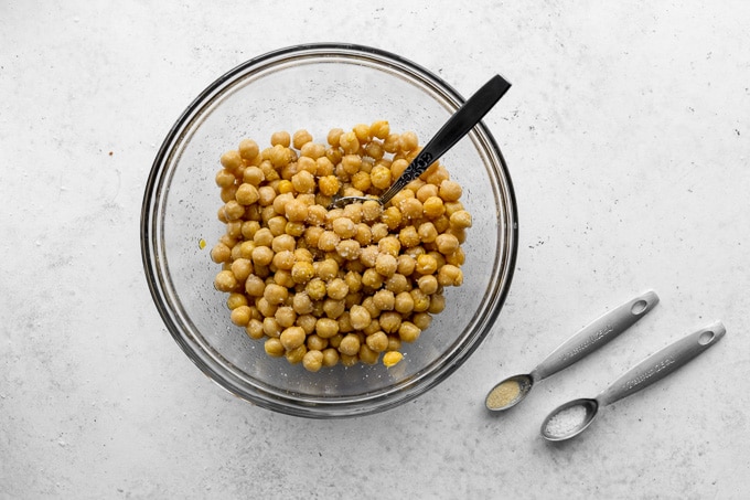 Chickpeas in a glass bowl with seasoning being stirred in.