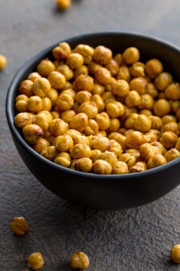 Air fryer chickpeas in a small black bowl with some chickpeas scattered around the bowl.