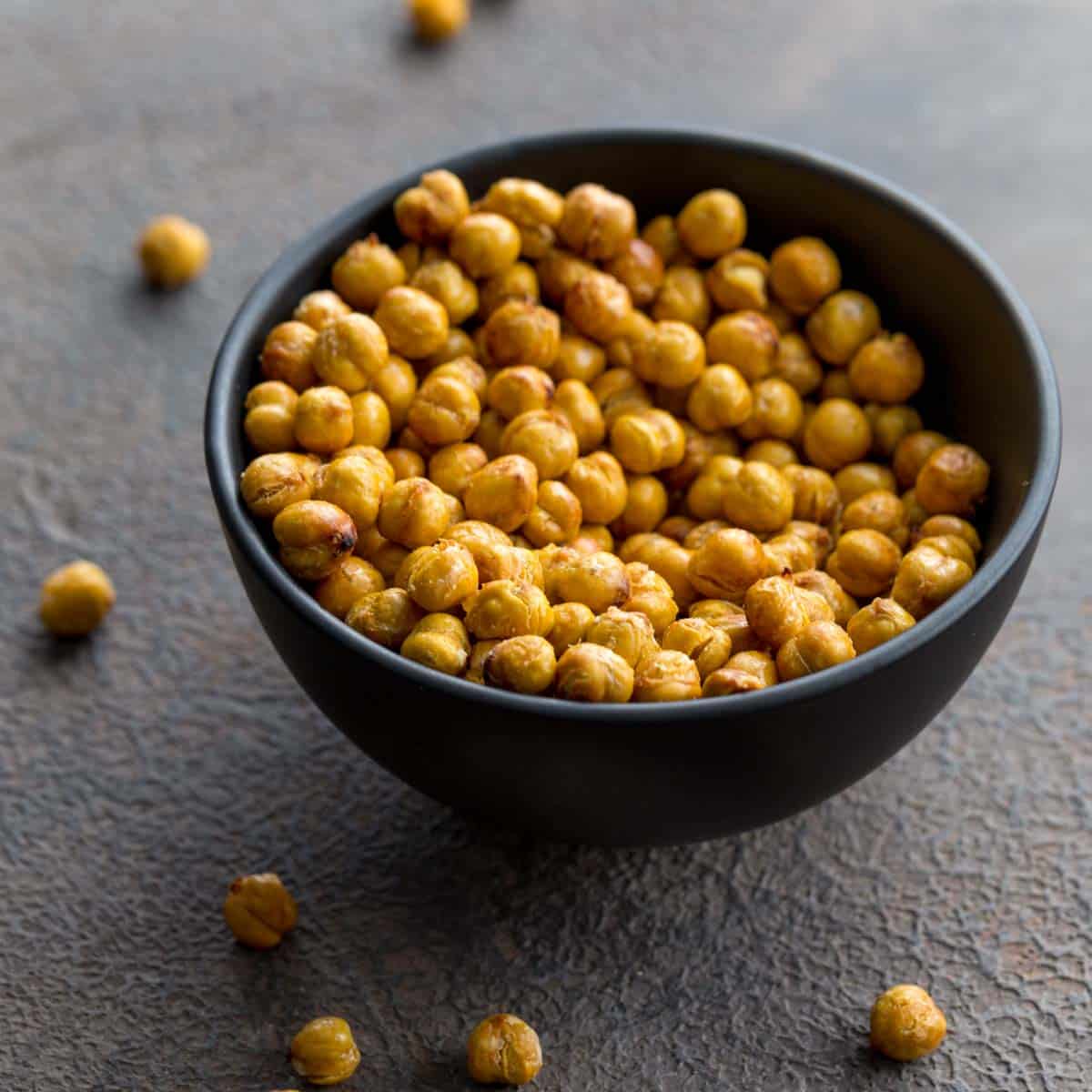 Air fryer chickpeas in a small black bowl with some chickpeas scattered around the bowl.