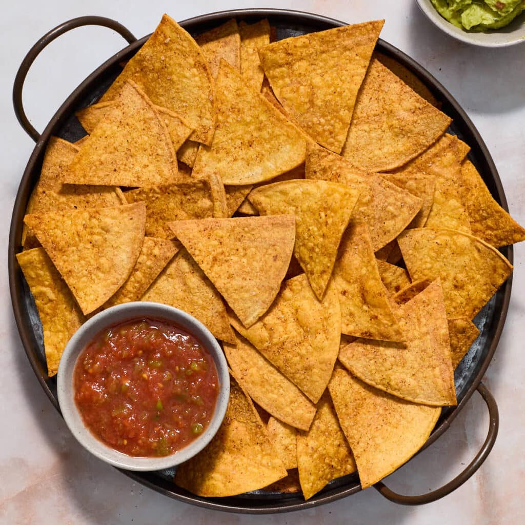 Air fryer tortilla chips served on a round platter with salsa and guacamole on the side.