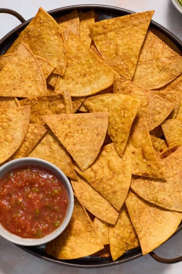 Air fryer tortilla chips served on a round platter with salsa and guacamole on the side.