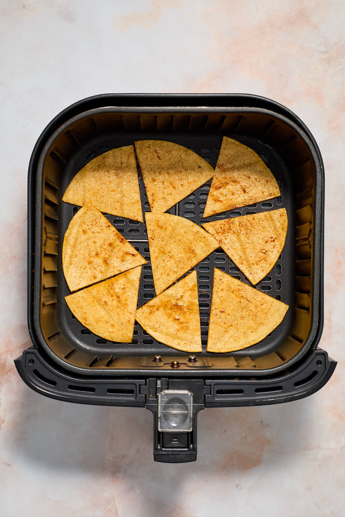 Tortilla triangles arranged in a single layer in the bottom of an air fryer basket.