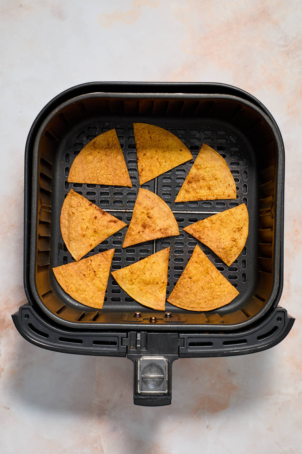 Air fried tortilla chips in an air fryer basket.