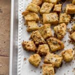Everything bagel seasoned croutons on a sheet pan lined with parchment paper.