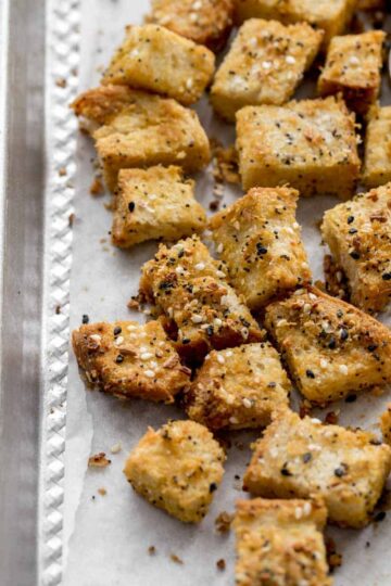 Everything bagel seasoned croutons on a sheet pan lined with parchment paper.