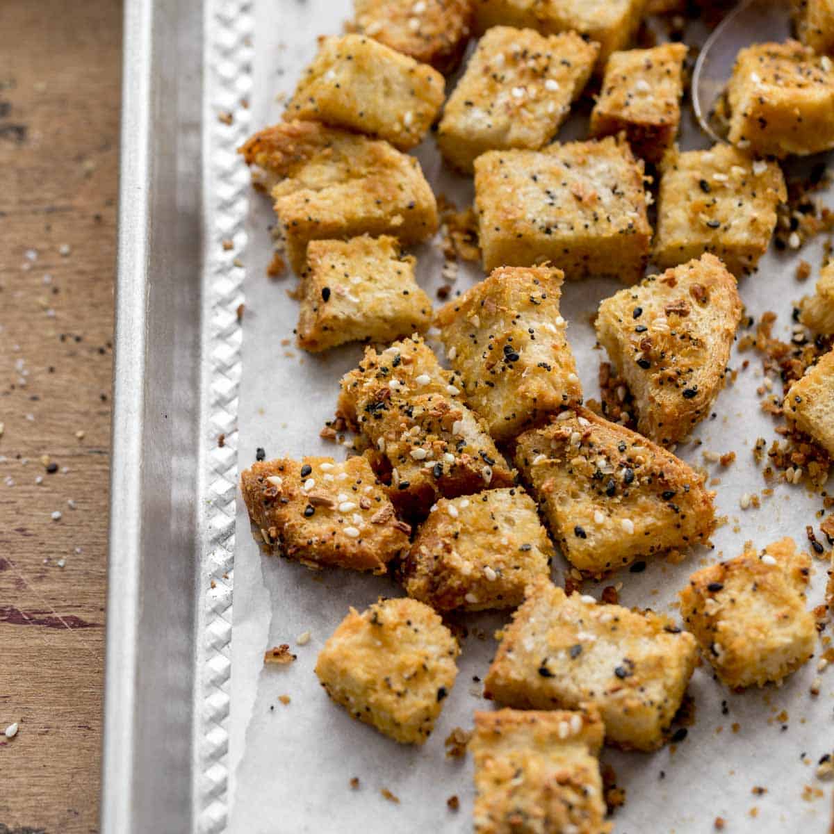 Everything bagel seasoned croutons on a sheet pan lined with parchment paper.