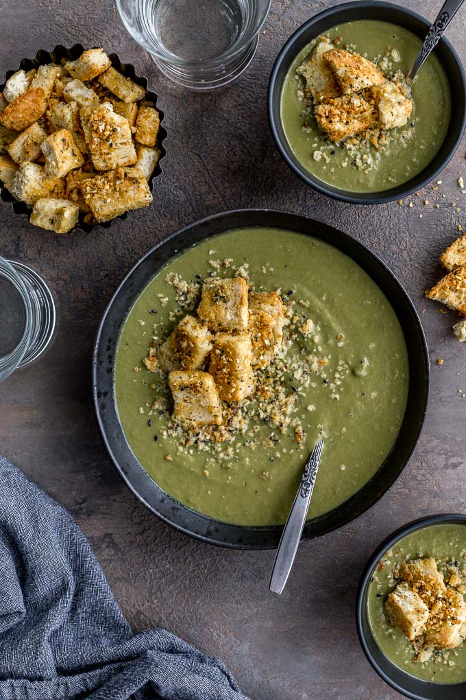 Overhead view of green pea soup in black bowls and topped with croutons.